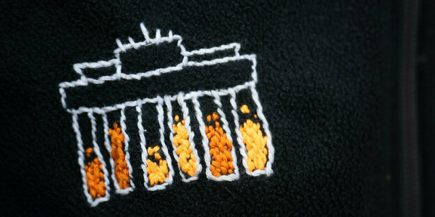 Ausschnitt: Gestickte Version auf des Brandenburger Tors in verschiedenen Orangetönen auf der Jacke eines Angeklagten
