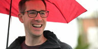 Ein Mann mit einem Regenschirm in der Hand lächelt in die Kamera