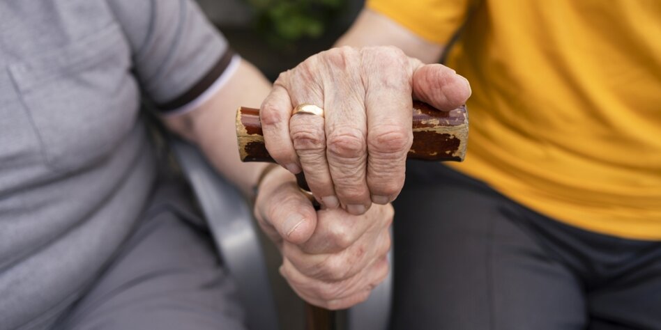 Hände eines sehr alten Ehepaares umklammern einen Gehstock