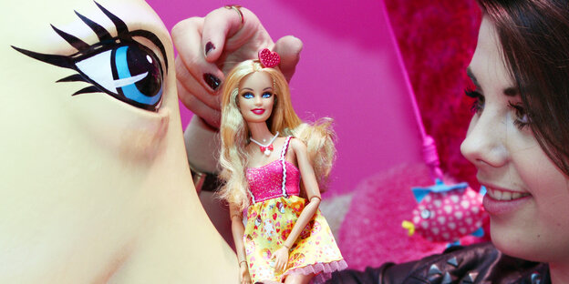 Eine Frau hält eine Barbiepuppe in die Kamera